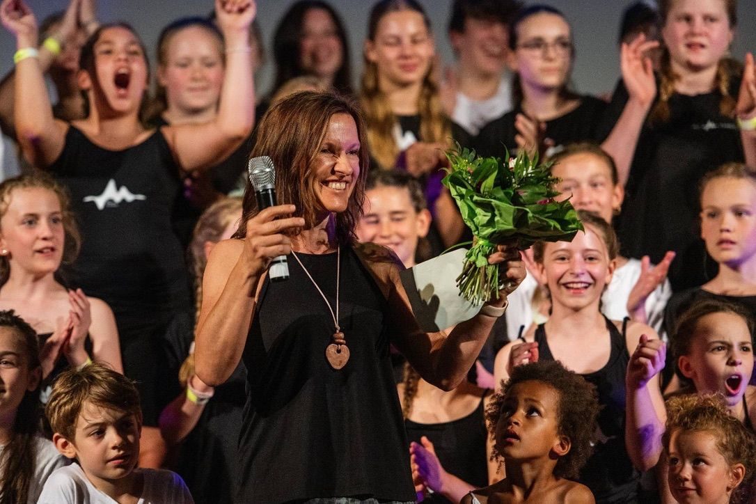 Monica Czech mit Mikrofon und Blumenstrauß, umringt von jubelnden Kindern