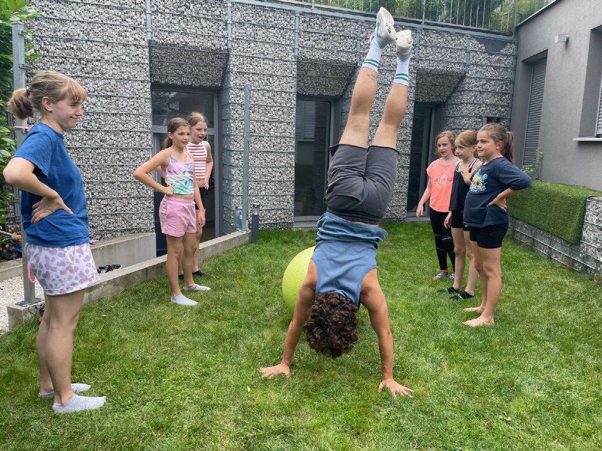 Ein Kind im Handstand auf der Wiese, die Gruppe schaut zu