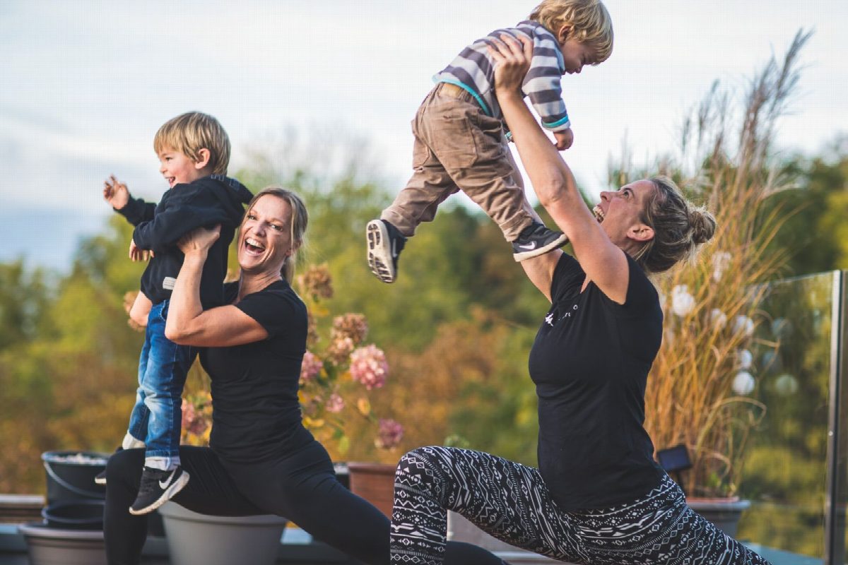 Zwei Frauen heben lachend ihre Kleinkinder beim Training hoch