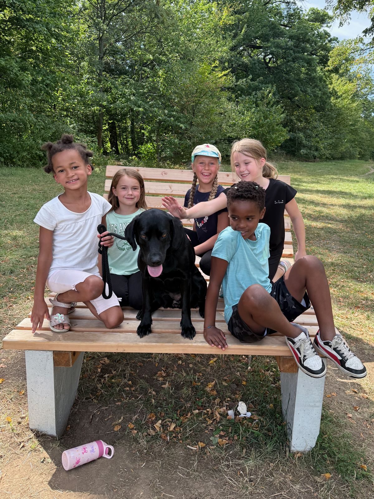 Fünf Kinder mit einem schwarzen Hund auf einer Holzbank